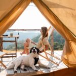Mujer relajándose en un deck con perro y paisaje montañoso.